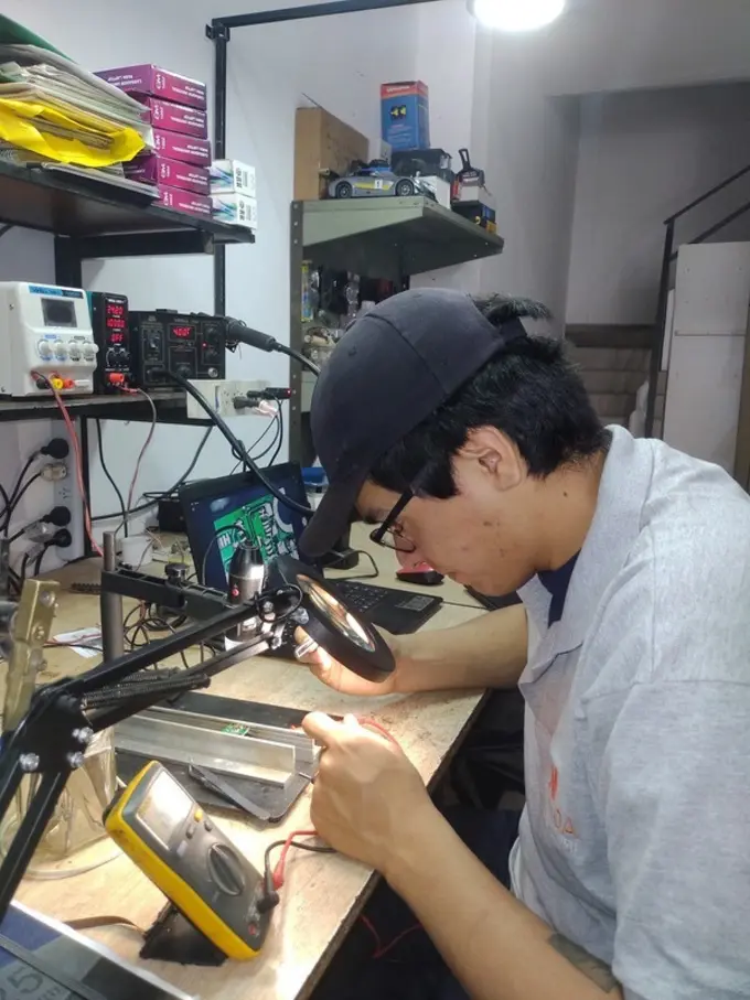 Técnico de ServiNOA diagnosticando una placa electrónica con lupa y multímetro